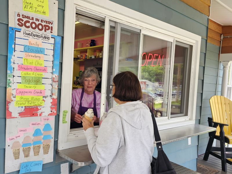 A woman serves an ice cream cone out of a window