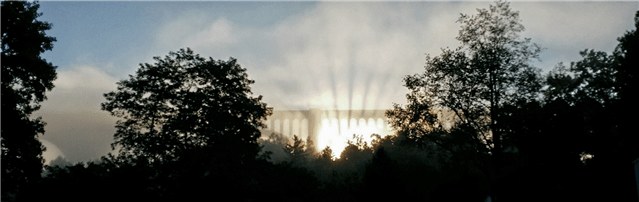 Grand Prize Winner: Rays of Sunshine PHOTOGRAPHER: Brandi Stull. Sun shine breaking through clouds in front of a bridge, with tress in the foreground.