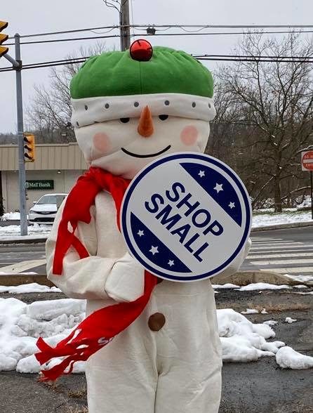 A snowman mascot holds a "Shop Small" sign outside of J.R's Hallmark