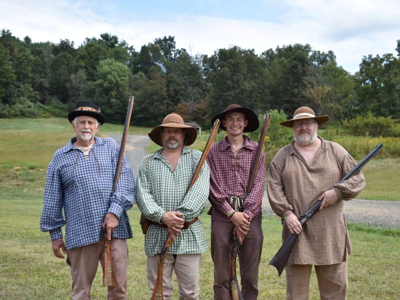 Men in frontier-style clothes hold old-fashioned muzzleloaders